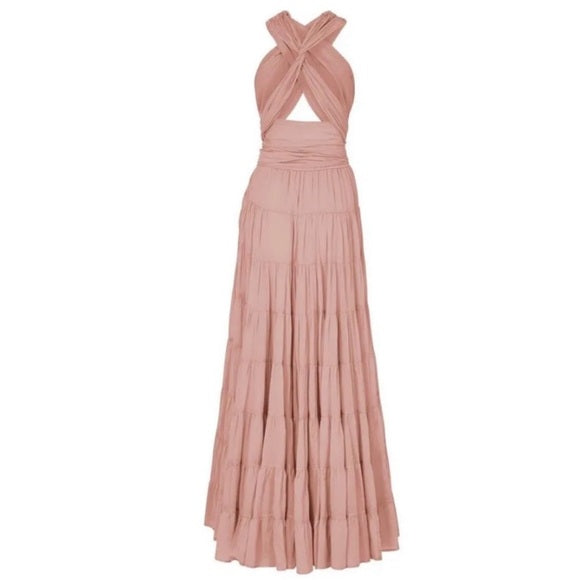 She's wearing a flowing, dusty rose or terracotta-colored maxi dress with a crisscross halter-style top and a high-waisted, belted skirt that has a tiered, ruffled design.